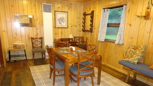 Une pièce aux murs lambrissés, comprenant une table à manger, des chaises, un banc, un tableau encadré et une fenêtre avec des rideaux.