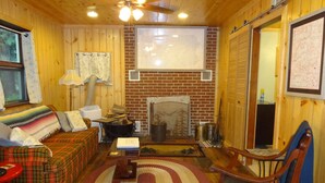 L’intérieur d’un chalet accueillant, avec un plafond en bois, une cheminée, un canapé, une table à manger et un fauteuil.