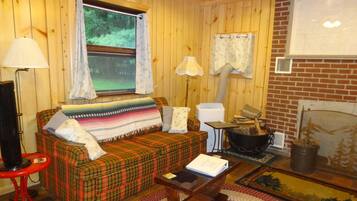 Ein gemütliches Blockhaushaus-Interieur mit einem karierten Sofa, einem roten Sessel, einem Holztisch, einem Kamin und einem Fenster mit Vorhängen.
