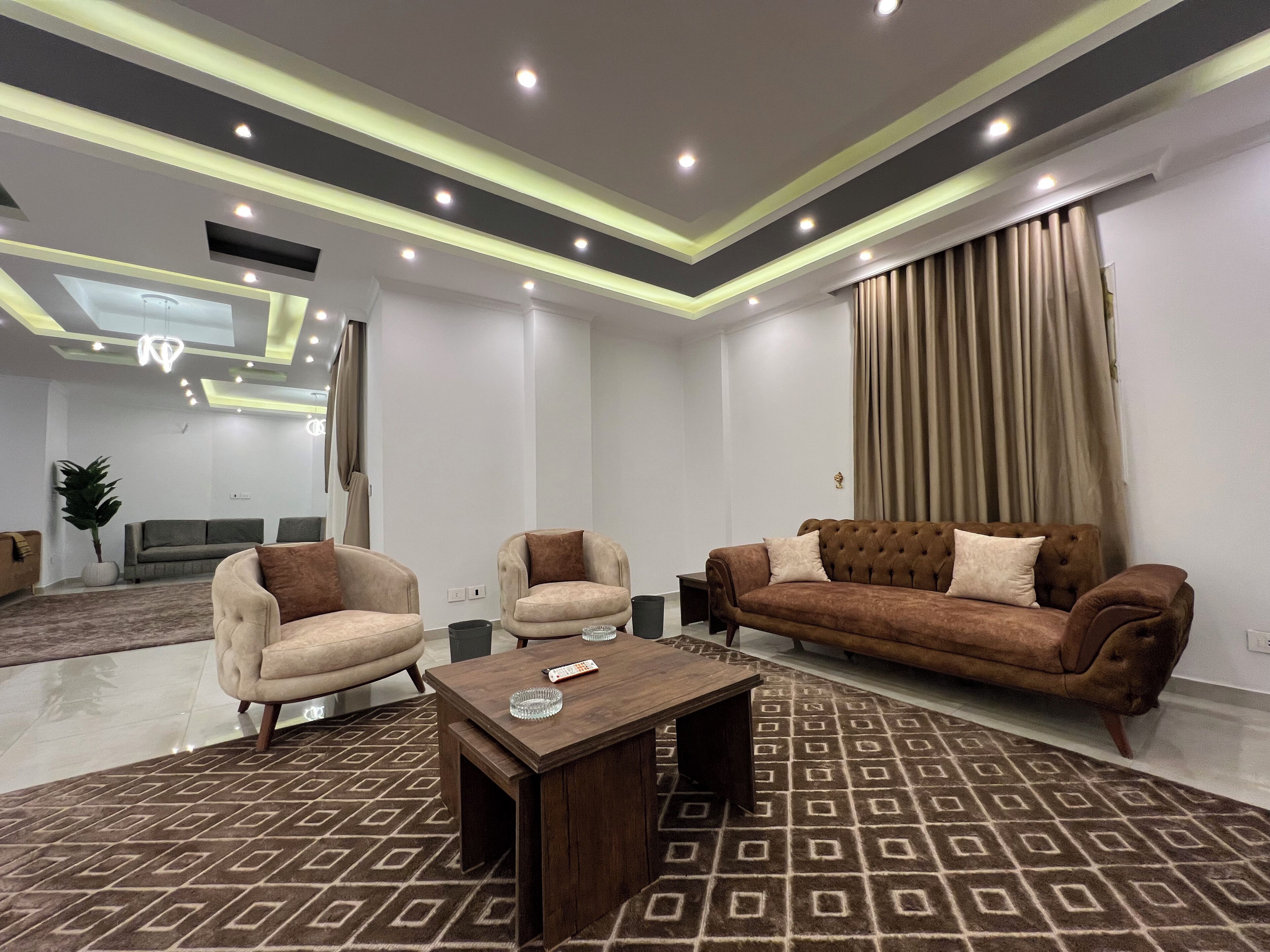 Una sala de estar moderna con una alfombra marrón estampada, un sofá marrón, dos sillones y una mesa de centro de madera.