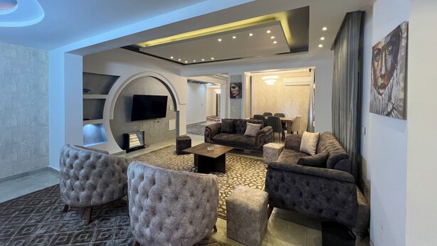 A modern living room with a sofa set, ottomans, a flat-screen TV, and a dining area. - ELITE Comfort 3BR Apartment New Cairo   (New Cairo)