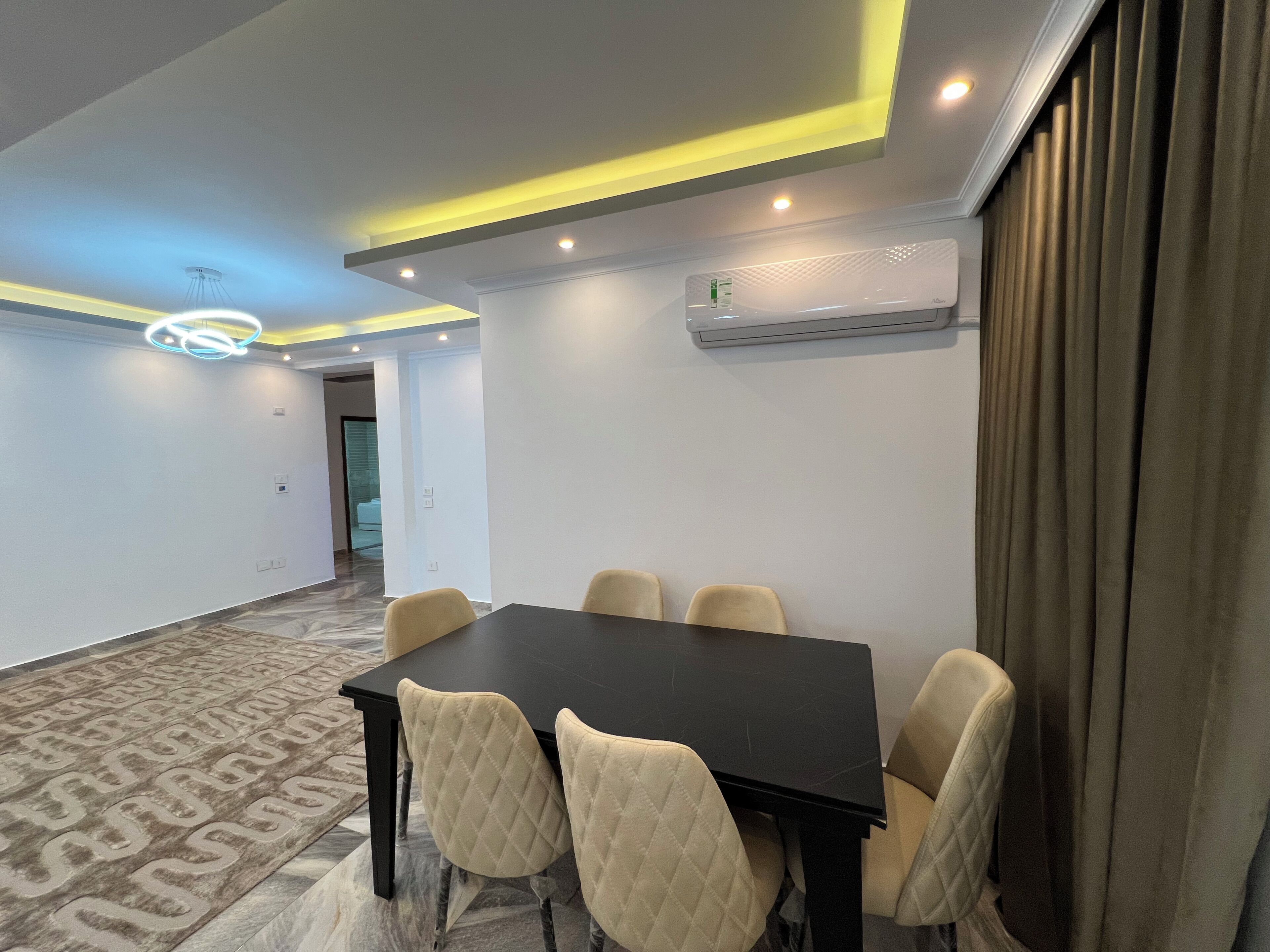 A conference room with a black table, beige chairs, recessed lighting, an air conditioning unit, and patterned carpet.