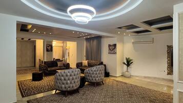 A modern living room with a circular ceiling light, sofas, a patterned rug, and a potted plant.