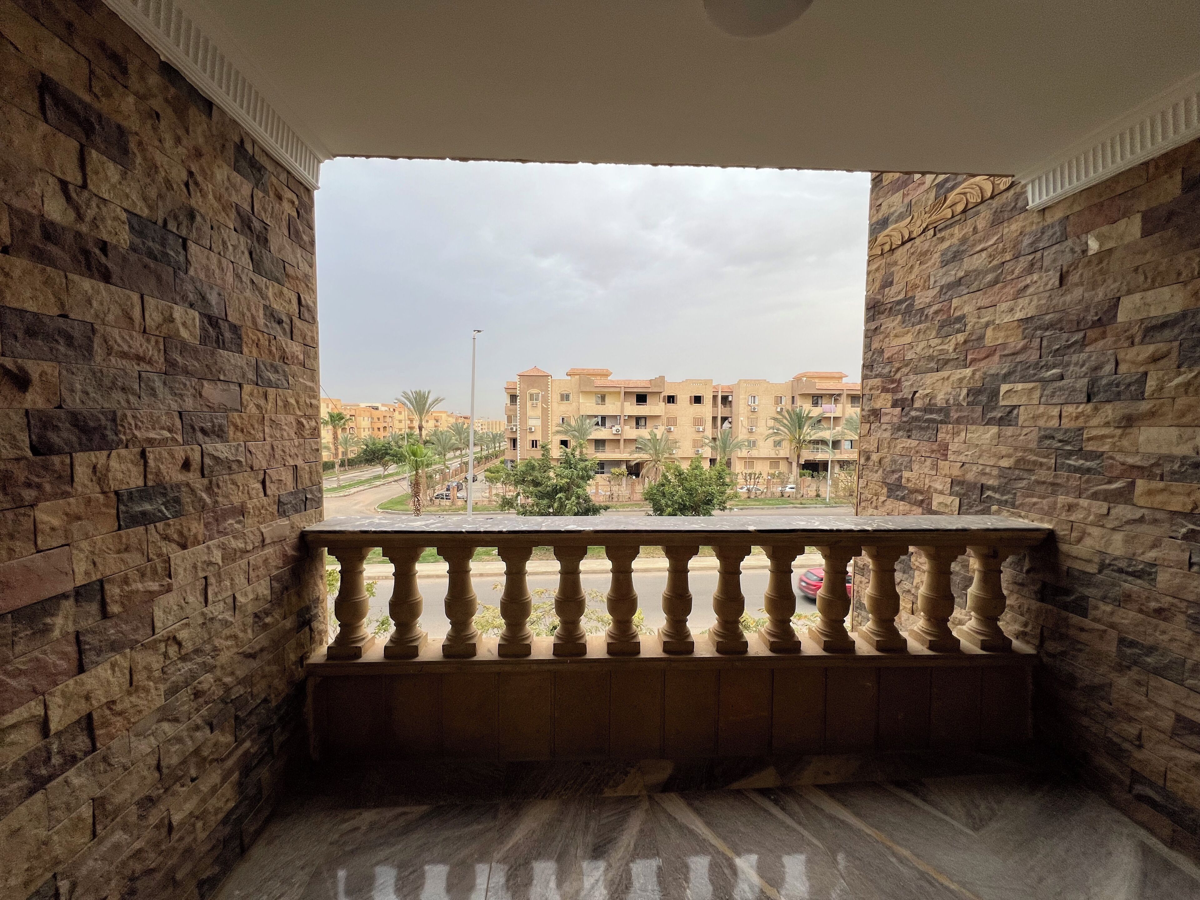A room with a stone wall, a marble floor, and a balcony with a balustrade.