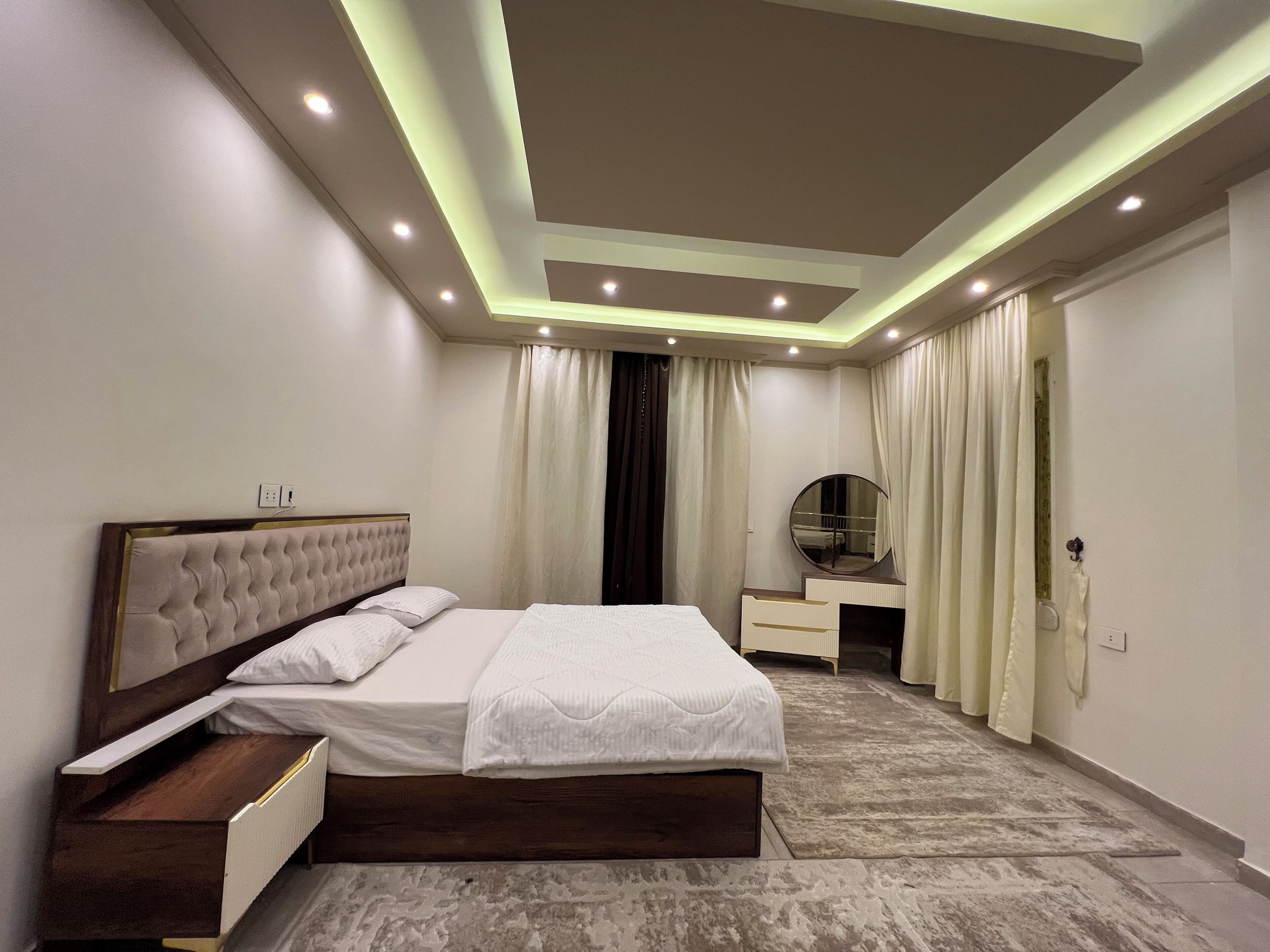 Une chambre moderne avec un lit, des tables de chevet, un miroir et un plafond doté d’un éclairage encastré.
