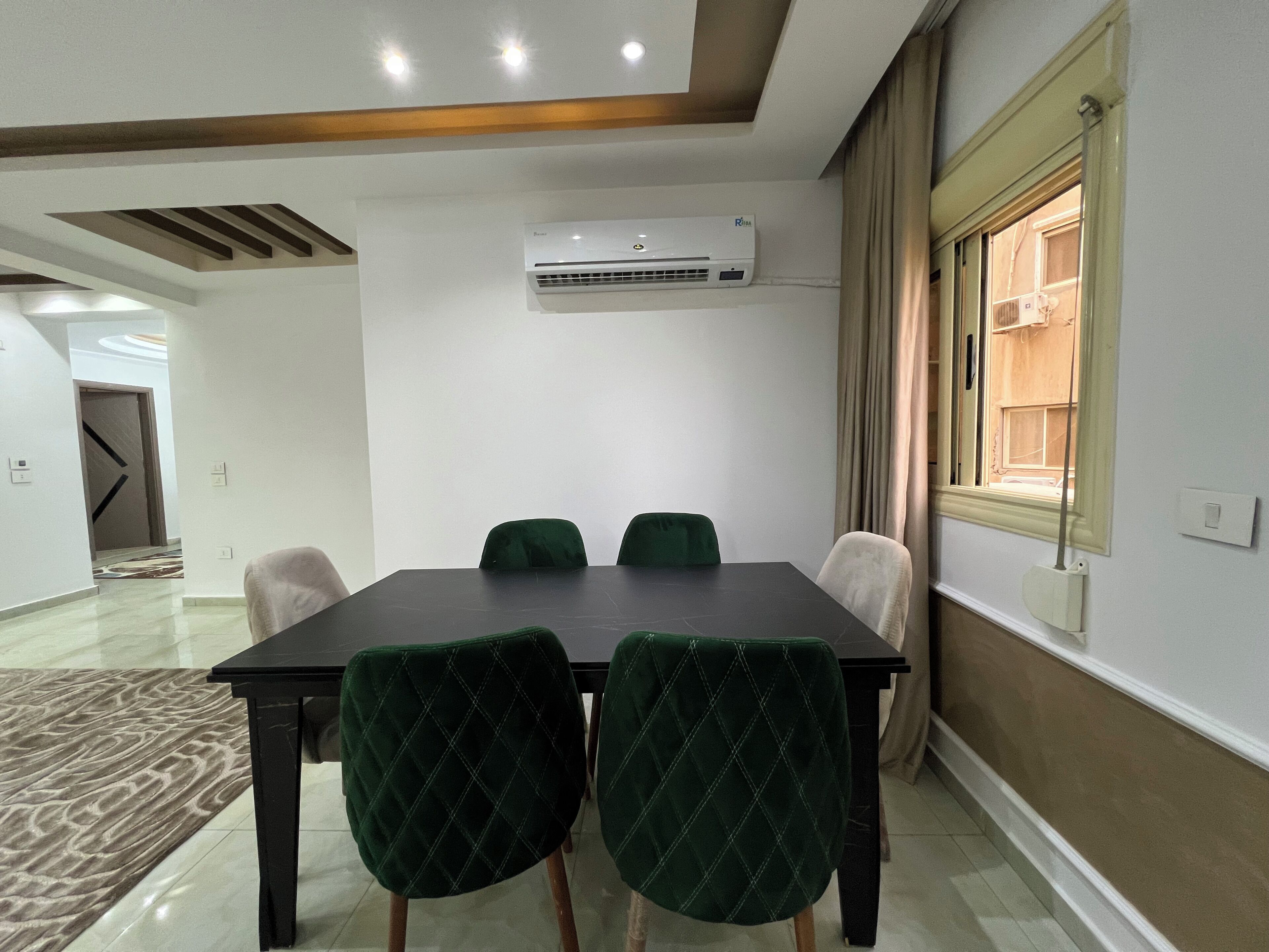 Une salle de conférence avec une table, quatre chaises, un appareil de climatisation, une fenêtre avec des rideaux et une porte au fond.