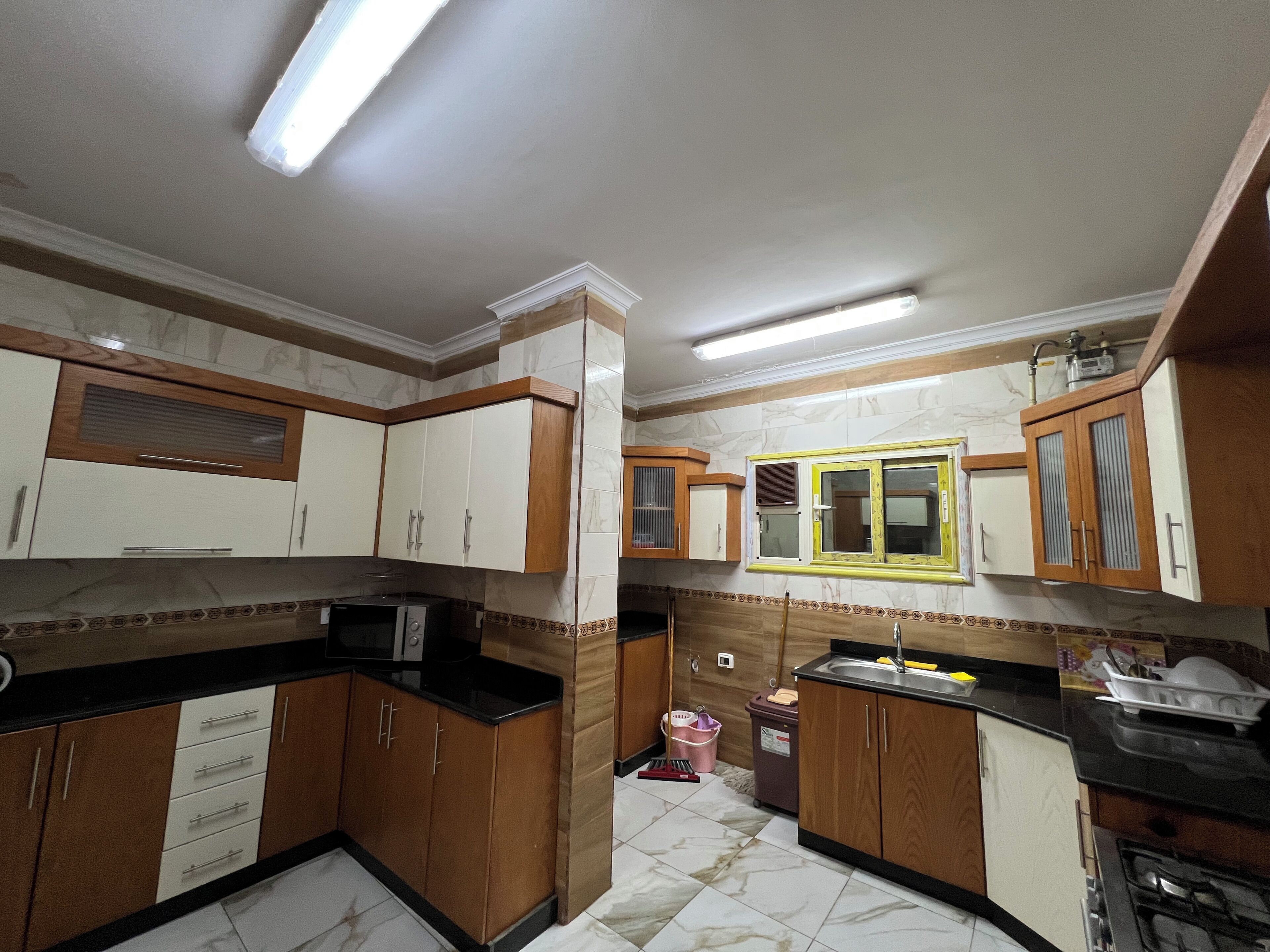 A kitchen with cabinets, a microwave, a sink, and a window with a yellow frame.
