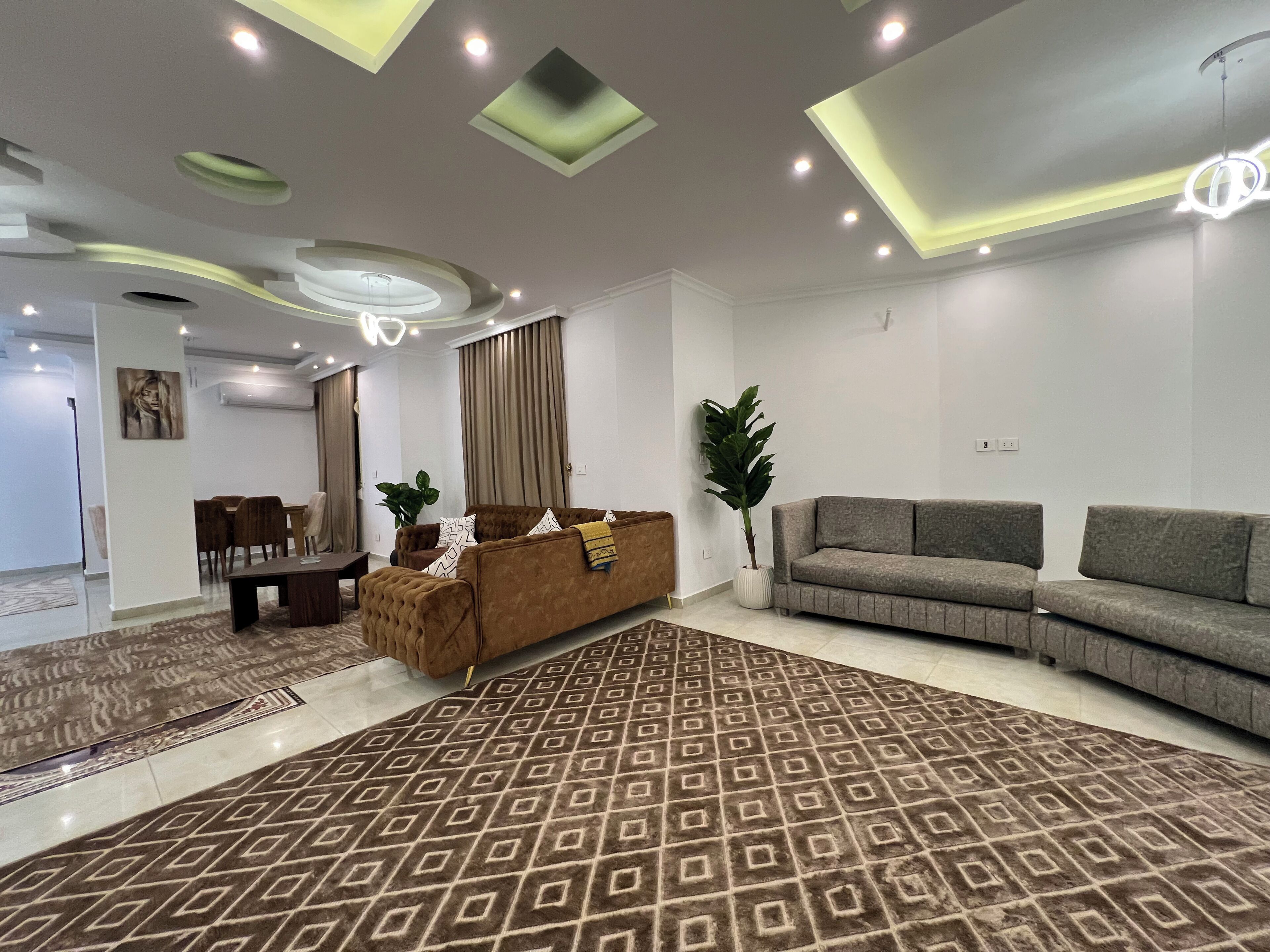 Una sala moderna con alfombra estampada, sofás, zona de comedor e iluminación empotrada en el techo.