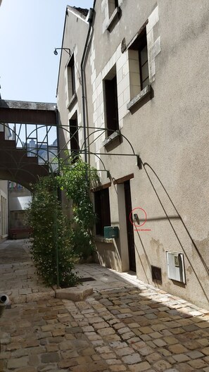 Un edificio con patio empedrado de piedra, una planta verde y un buzón de seguridad.
