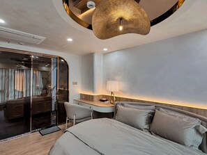 Et moderne hotelværelse med seng, skrivebord, stol og en unik, cirkelformet lampe.