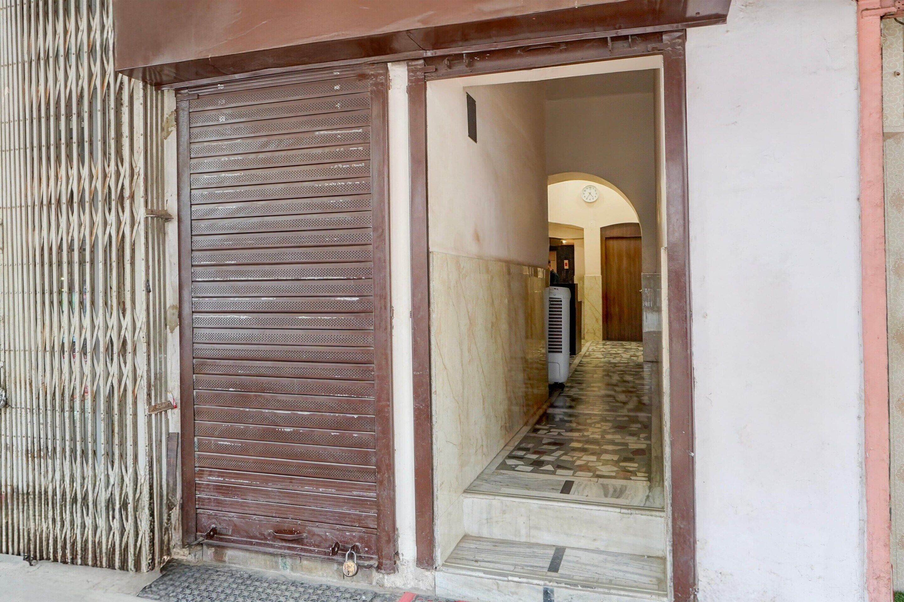 A closed metal shutter door, a tiled staircase, and a hallway leading to an interior space.