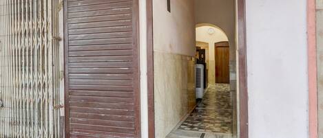 A closed metal shutter door, a tiled staircase, and a hallway leading to an interior space.