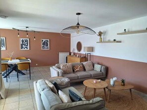 A living room with a sofa, two coffee tables, a dining area with chairs, and a TV on the wall. - Villa portiragnes between land and sea (Portiragnes)