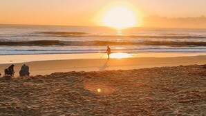 A beach scene with a person walking along the shore, waves, and a sunset. - Beach Retreat 3BR/2BA – Across Paradise Park, Melbourne FL (Melbourne)