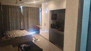 Une chambre d’hôtel moderne équipée d’un lit, d’un petit bureau, d’une kitchenette et d’une grande fenêtre avec des rideaux.