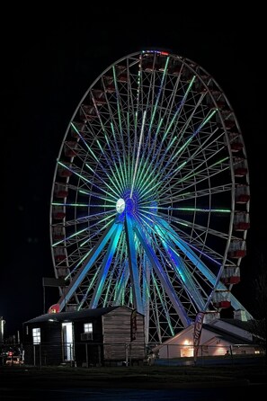 A large Ferris wheel with a central hub and multiple cabins, surrounded by a fence and a building with a sloped roof. - Lakes, Links, and Luxury at The Landing Overlook!  Private Balcony w/ Sunsets! (Branson)