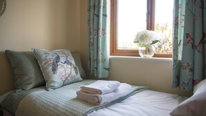 Un lit bien fait, avec des oreillers, une fenêtre avec des rideaux et un vase rempli de fleurs posé sur le rebord de la fenêtre.