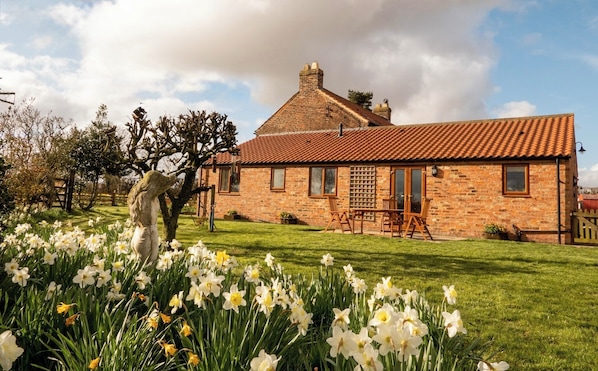 A brick house with a tiled roof, a lawn with daffodils, and a statue.