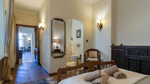 Une chambre d’hôtel comprenant un lit, une tête de lit en bois, une table de chevet, un miroir, une salle de bain avec des toilettes et un lavabo, et un couloir menant à un espace repas.
