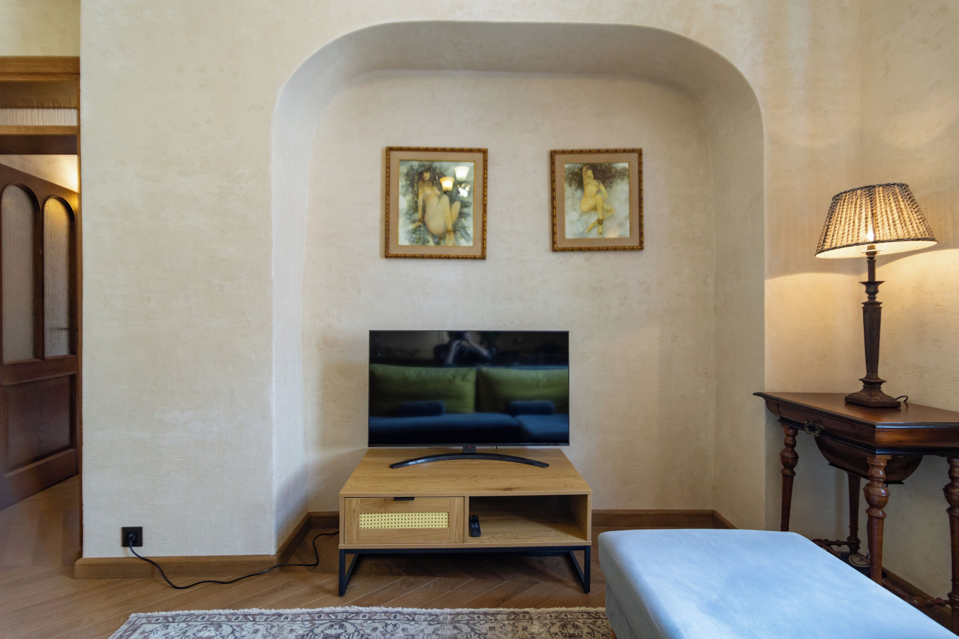 Ein Wohnzimmer mit Fernseher, zwei gerahmten Kunstwerken, einer Lampe und einem Sofa.