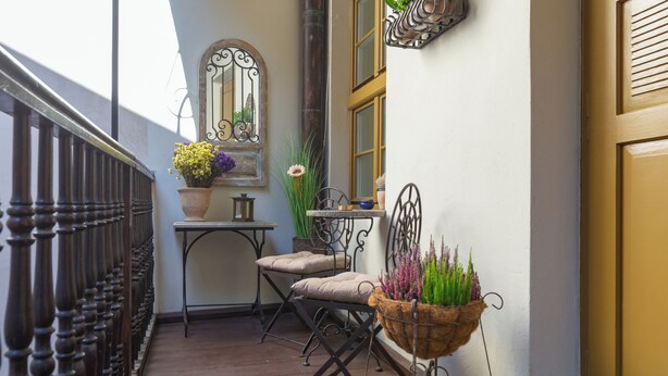 Un balcon avec une balustrade en bois, une petite table avec une chaise et des plantes en pot.