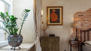 Une pièce comprenant un lit, une table de chevet, une armoire, une plante en pot, un tableau encadré et une fenêtre avec des rideaux.
