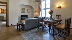 Un salon comprenant un canapé, une table à manger, des chaises, un lustre, des œuvres d’art accrochées au mur et un téléviseur.