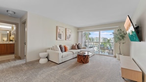 A spacious living room with a white sofa, a coffee table, and a large window offering a view of the city. - The Sail & Sky Suite - Chic 2BR Elegance with Stunning Marina Panoramas (Marina del Rey)