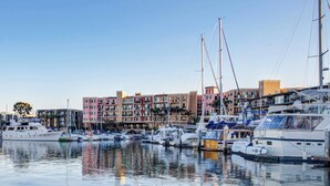 A marina with multiple boats docked, buildings in the background, and calm water reflecting the boats. - The Sail & Sky Suite - Chic 2BR Elegance with Stunning Marina Panoramas (Marina del Rey)