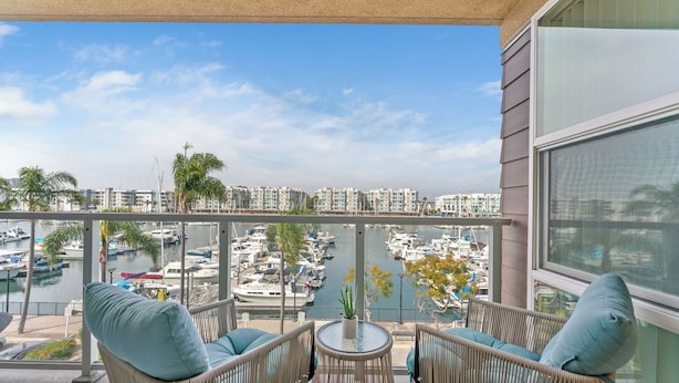 A balcony with wicker furniture, a small table, and a view of a marina with boats. - The Sail & Sky Suite - Chic 2BR Elegance with Stunning Marina Panoramas (Marina del Rey)