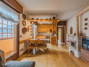 Eine gemütliche Küche mit Holzausstattung, einem Esstisch mit Stühlen, einem Kamin und einem Fernseher.