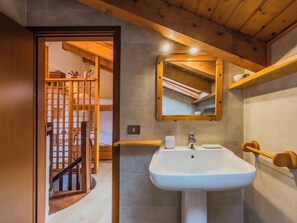 Une salle de bain avec un plafond en bois, un lavabo blanc, un miroir et une porte en bois.
