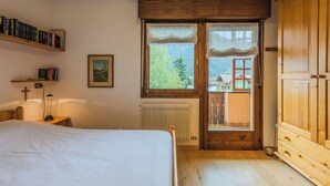 Een slaapkamer met een bed, een houten garderobe, een raam met uitzicht op een huis, een radiator en een boekenkast met boeken.