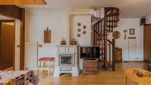Een woonkamer met een open haard, een houten trap, een televisie en een eethoek.