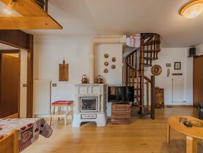 Ein Wohnzimmer mit Kamin, einer Holztreppe, einem Fernseher und einem Essbereich.