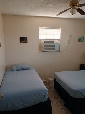 A bedroom with two beds, a ceiling fan, an air conditioning unit, and a window.