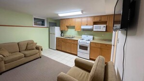Un espacio habitable compacto con kitchenette, un sofá, un televisor de pantalla plana montado en la pared y una lámpara en el techo.