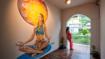 Una habitación con un mural de una figura meditativa, un balcón con vistas a edificios y una planta en maceta.