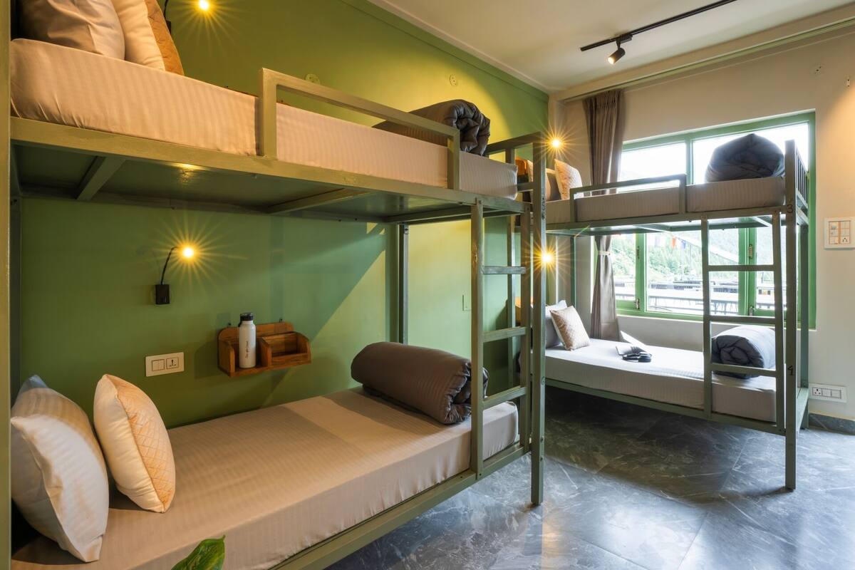 A bunk bed room with a green wall, a window with a view, and a shelf with a water bottle.