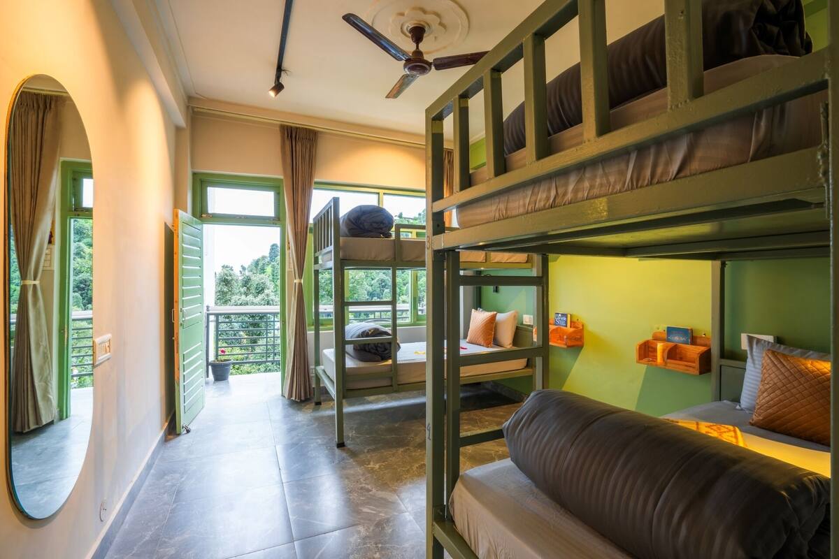 A bunk bed room with a ceiling fan, a sofa, and a view of greenery outside.