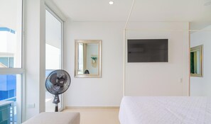 Ein modernes Schlafzimmer mit einem Bett, einem Standventilator, einem großen Spiegel und einem Fernseher an der Wand.