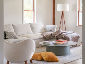 A living room with a sofa, a round coffee table, a lamp, and a window.