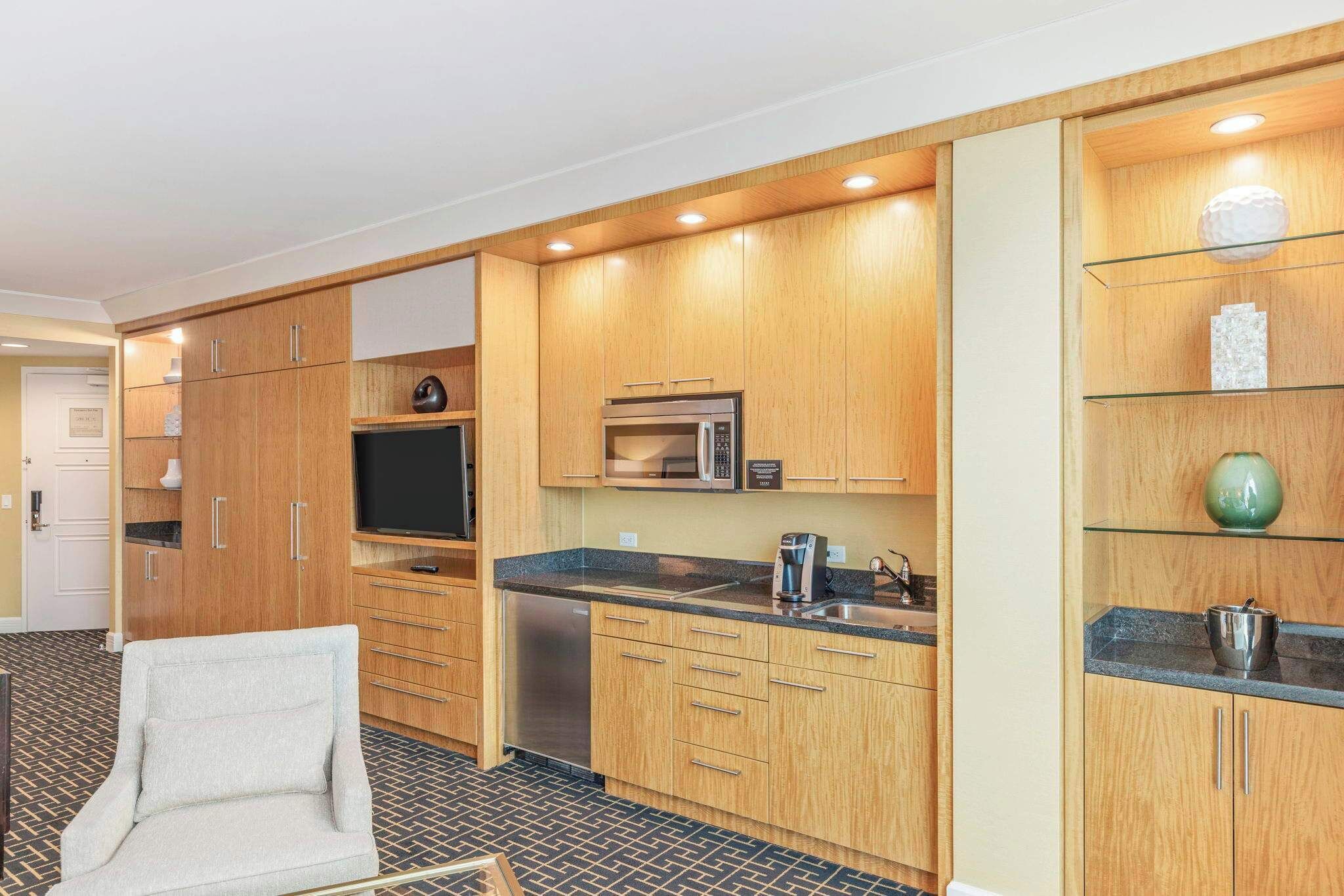 A compact kitchen with wooden cabinets, a microwave, a coffee maker, and a built-in oven.