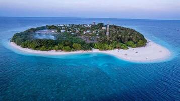 Vista aérea de una isla tropical con playa, vegetación densa y algunos edificios.