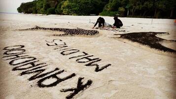 A beach with sand art spelling out 'KIRINDU' and two people in the background.