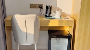 A hotel room with a desk, a chair, a coffee maker, a glass pitcher, and a mini-fridge. - Silver Bay Kamadhoo (Kamadhoo)