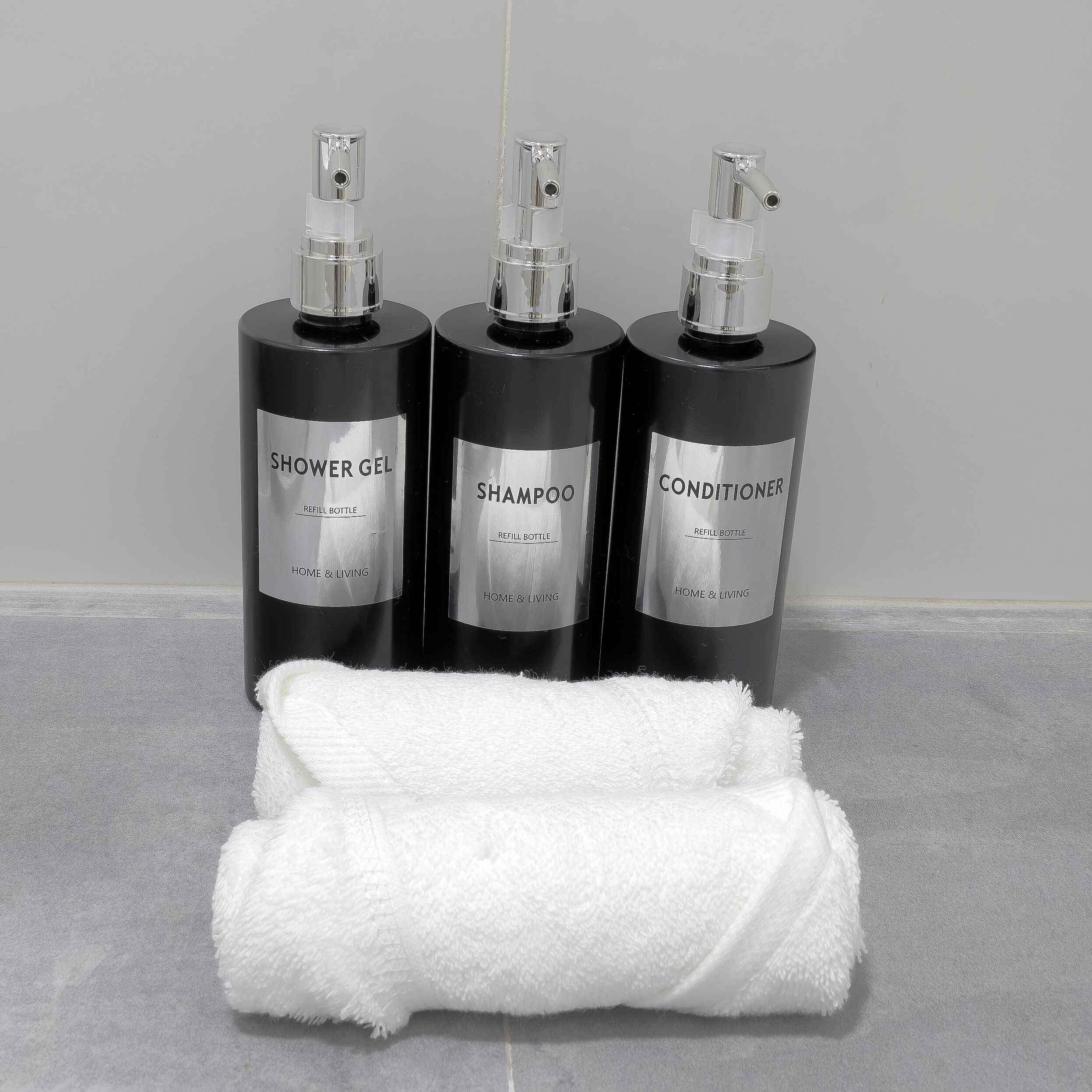 Tres botellas reutilizables de gel de ducha, champú y acondicionador sobre una encimera de baño.