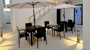 A spacious indoor area with a dining table, chairs, and umbrellas, a staircase, and a fire extinguisher. - Silver Bay Kamadhoo (Kamadhoo)