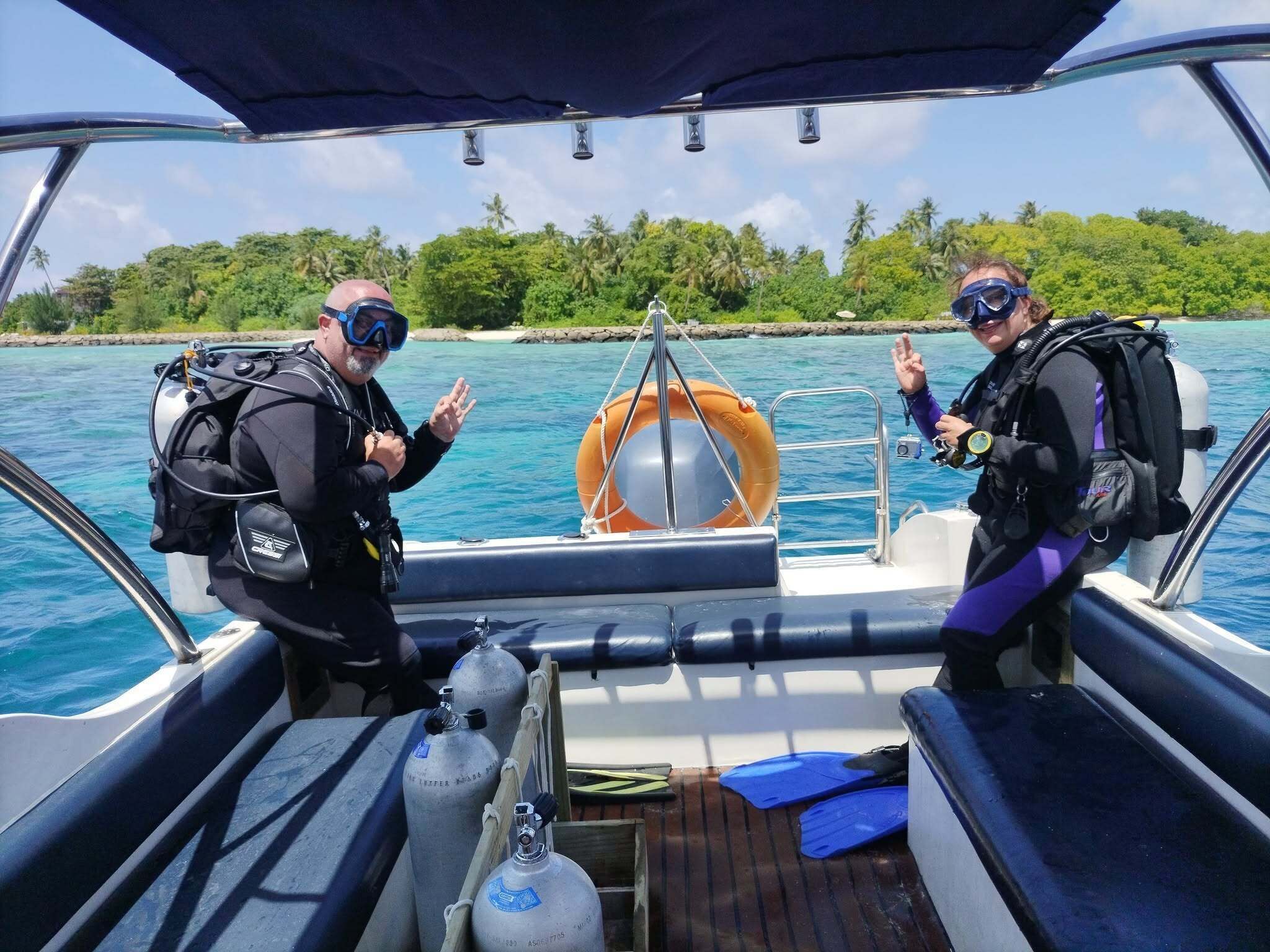 A boat with two scuba divers, a life preserver, and scuba tanks on deck.