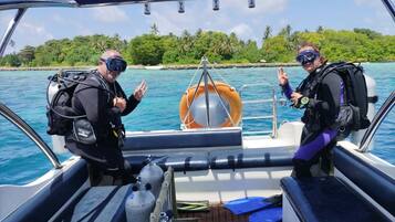 A boat with two scuba divers, a life preserver, and scuba tanks on deck.